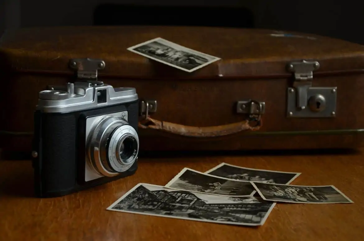 a film camera, photo prints and luggage as a reminder to take photographs for 30 Easy Pro Travel Tips You Should Be Following
